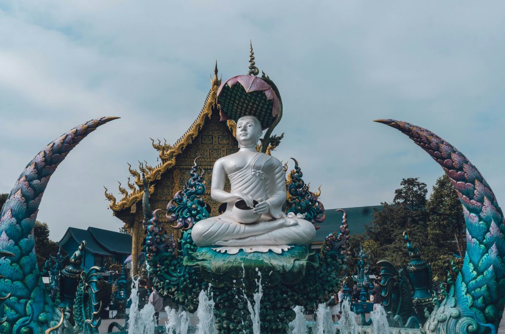 Wat Rong Suea Ten (Blue Temple) in Chiang Rai, Thailand, with a white seated Buddha statue and vivid blue-and-gold decorative sculptures.