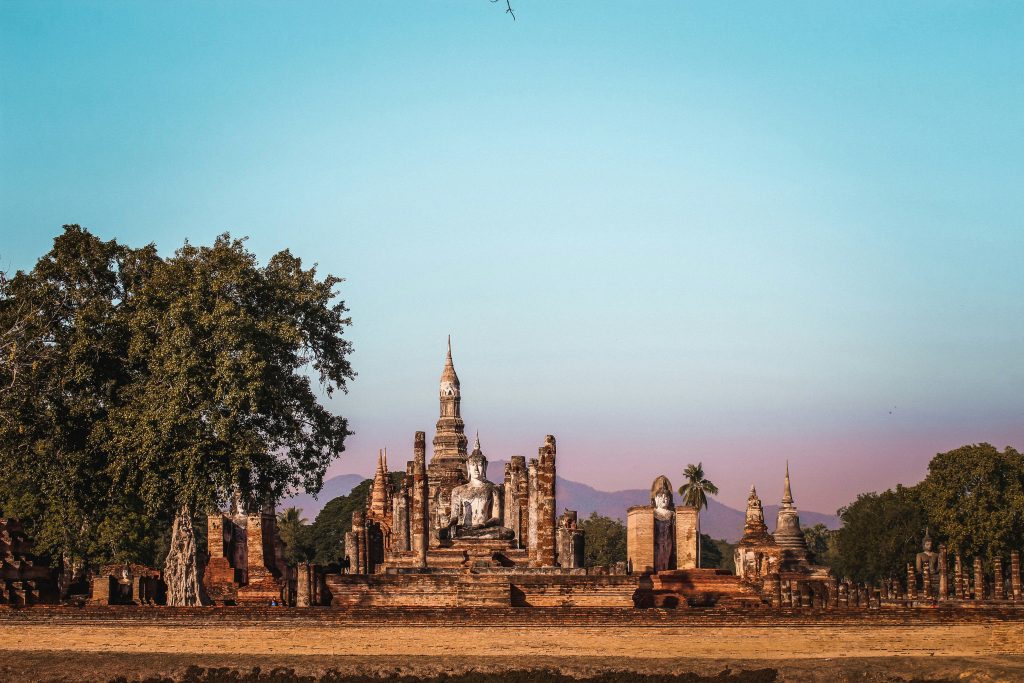 Sukhothai Historical Park in Thailand with ancient temple ruins, stone Buddha statues, and brick stupas at sunset.