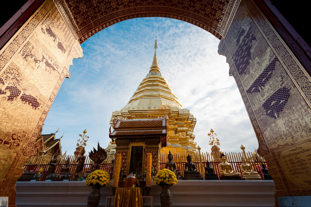 Wat Phra That Doi Suthep in Chiang Mai, Thailand, with the golden chedi framed by ornate temple doors and Buddha statues.