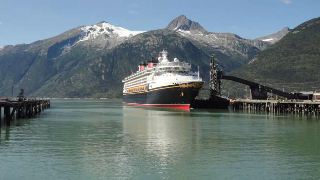 Large passenger ship docked in an Alaska coastal harbor with mountains behind