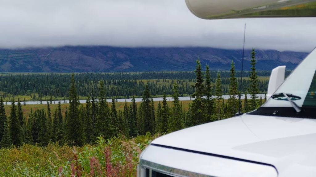 Car parked at scenic overlook in Alaska with forest and mountains in background