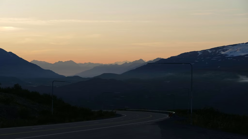 Curving highway in Alaska at sunset with layered mountain silhouettes